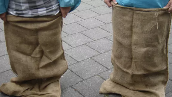 2 kinderen staan met hun benen in een jutezak en houden hem vast, klaar om te springen