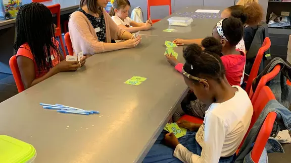 kinderen en animator rond de tafel met kaartjes in hun hand
