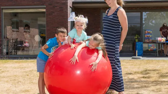 3 kinderen leunen en zitten op de reuzebal