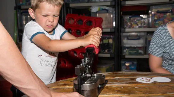 Torre duwt de hendel van de buttonmachine naar beneden en je ziet aan zijn gezicht dat hij hard moet duwen.