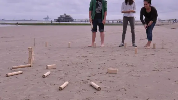 3 jongeren spelen viking kubb op het strand