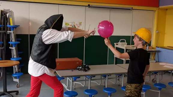 goochelaar prikt geblinddoekt een ballon stuk die wordt vastgehouden door een deelnemer