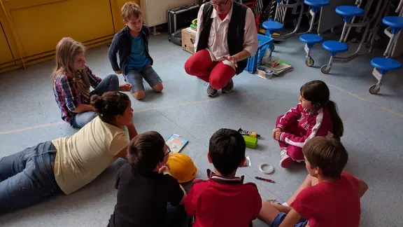 kinderen zitten in een kring en kijken naar de goochelaar