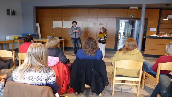 deelnemers zitten aan een tafel en kijken voor zich naar 2 andere deelnemers die iets voortonen