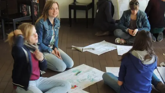 enkele deelnemers zitten op de grond met een groot blad met tekeningen op