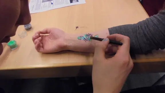 iemand plaatst een glittertattoo bij iemand anders