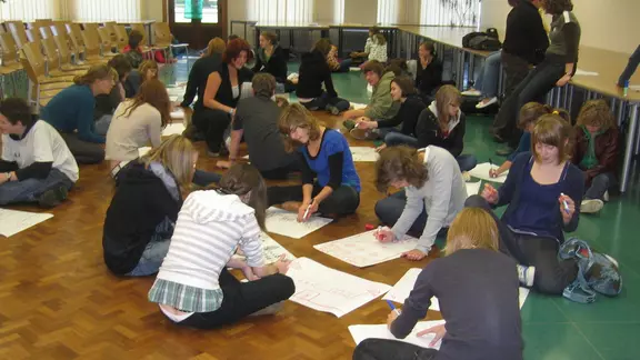 deelnemers zitten in groepen op de grond met papier bij zich en tekenen