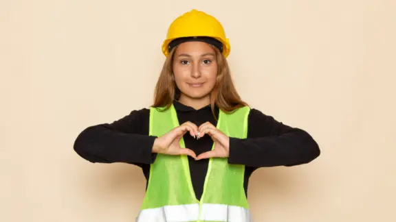 vrouw met fluojas en helm vormt een hartje met haar handen