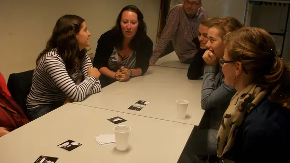 deelnemers zitten aan een tafel met kaartjes in het midden