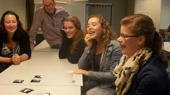 deelnemers zitten aan een tafel met kaartjes in het midden en glimlachen