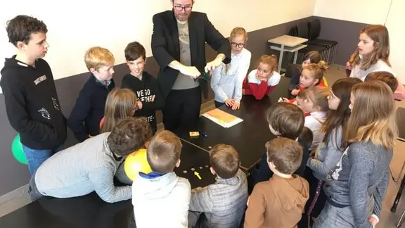 kinderen rond een tafel met goochelaar filip