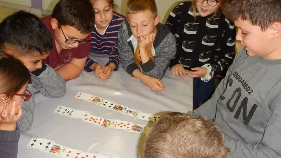 kinderen rond een tafel oefenen een kaartentruc