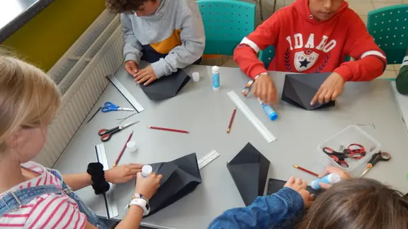 4 kinderen zitten aan een tafel een knutselen een goocheltruc