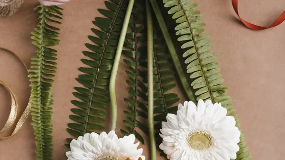 iemand knoopt een drietal bloemen aan elkaar met een rood lint