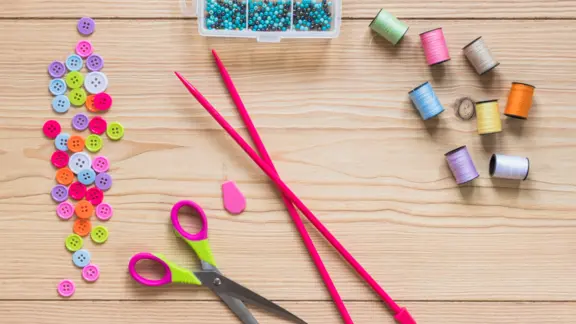 er liggen breinaalden, knopen, een schaar en bollen garen op de tafel