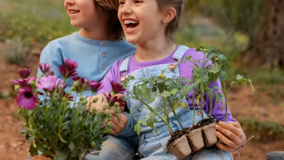 2 kinderen zitten in de aarde en houden bloemen vast. ze lachen