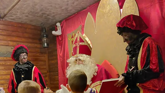 Sint leest uit zijn boek voor aan 2 kinderen, 2 pieten staan er bij