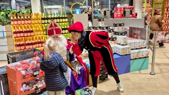 Sint en Piet spreken tegen een kindje die in een warenhuis komt winkelen