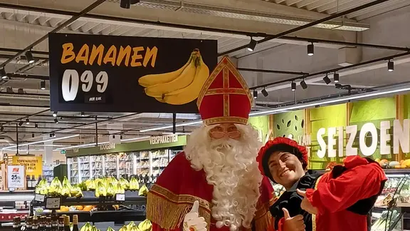 Sint en piet poseren voor de foto. Boven hun hoofd hangt reclame voor bananan.