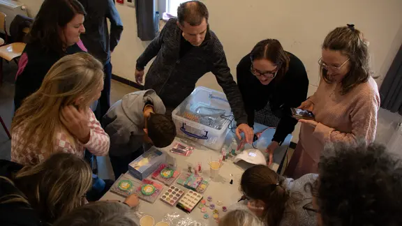 Een tiental deelnemers staat rond een tafel te kijken naar hoe je een epoxy sleutelhanger maakt