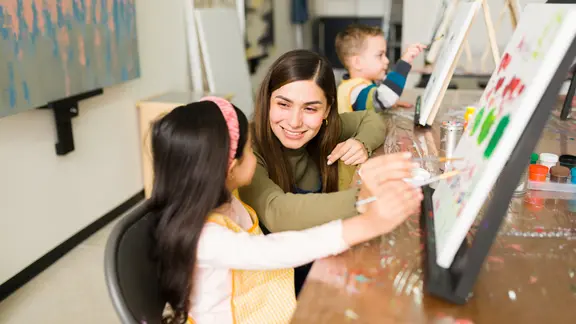 Een kind en een jongere (animator) schilderen samen