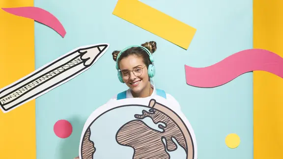 een meisje zit op een stoel en houdt een wereldbol vast. Er staan potloden en slingers als versiering