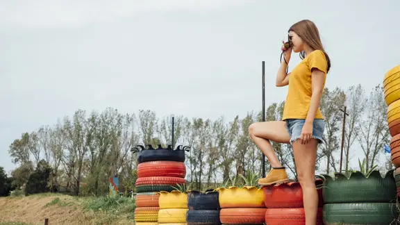 Tiener kijkt door een verrekijker en staat in een open buitenruimte met autobanden